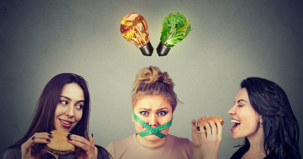 10 Most Unbelievable Metabolism Myths That You Should Know By Now | metabolism myths women eating hamburgers looking at a stressed chubby girl with measuring tape around her mouth metabolism myths - women eating hamburgers looking at a stressed chubby girl with measuring tape around her mouth
