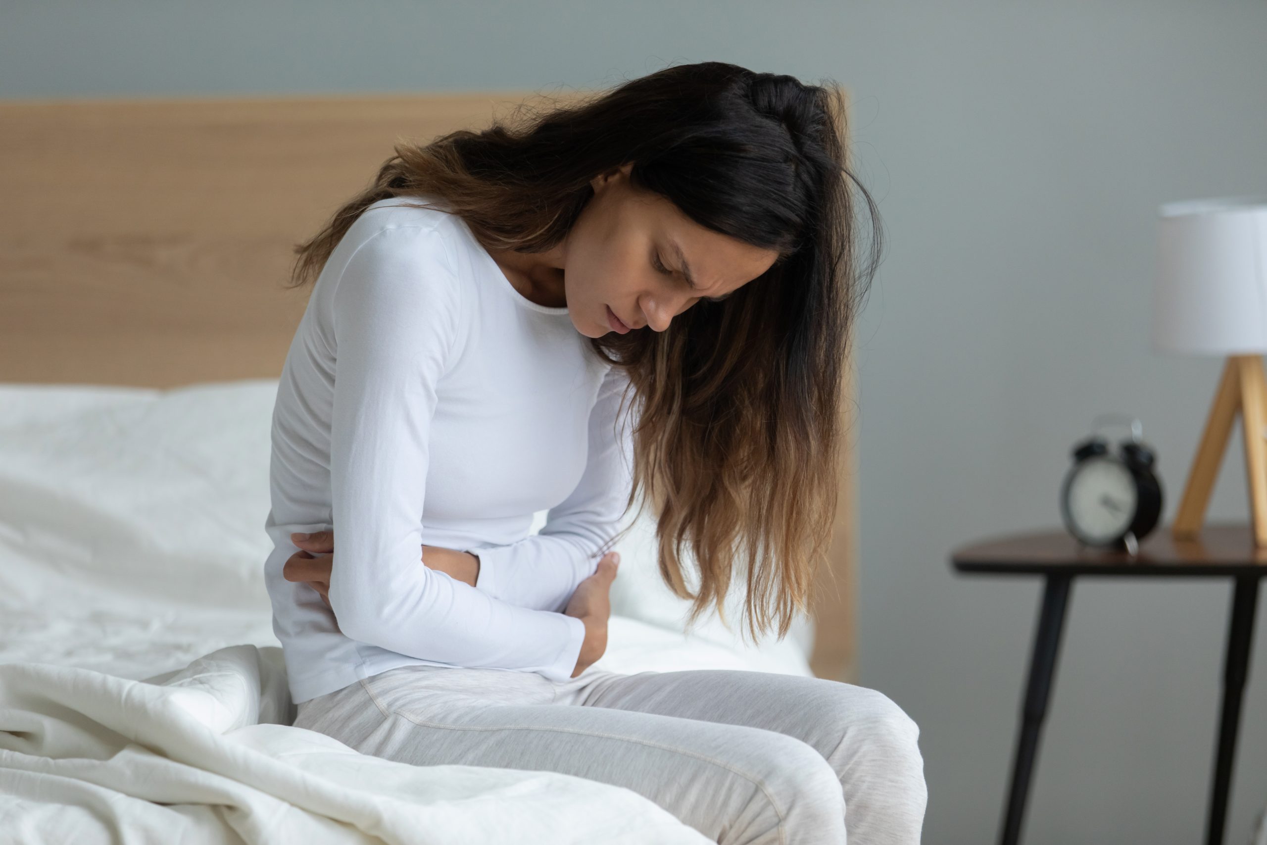 Beyond the Thyroid: The Thyroid German New Medicine Impact on Hashimoto's And Thyroid Symptoms | Thyroid German New Medicine Unhealthy woman sit on bed touching her stomach scaled Thyroid German New Medicine - Unhealthy woman sit on bed touching her stomach