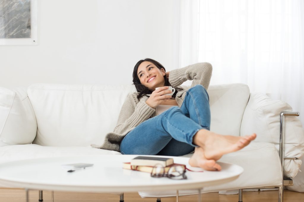 Cycle Mapping: The Best Foods, Workouts And Supplements for Your Cycle | Cycle Mapping Young smiling woman sitting on sofa and looking up while drinking hot tea Cycle Mapping - Young smiling woman sitting on sofa and looking up while drinking hot tea