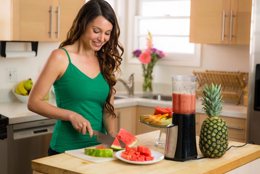 The Top 3 Essentials to Balance Hormones Naturally | balance hormones naturally woman home in kitchen making a smoothie with blender fresh fruits balance hormones naturally - woman home in kitchen making a smoothie with blender fresh fruits