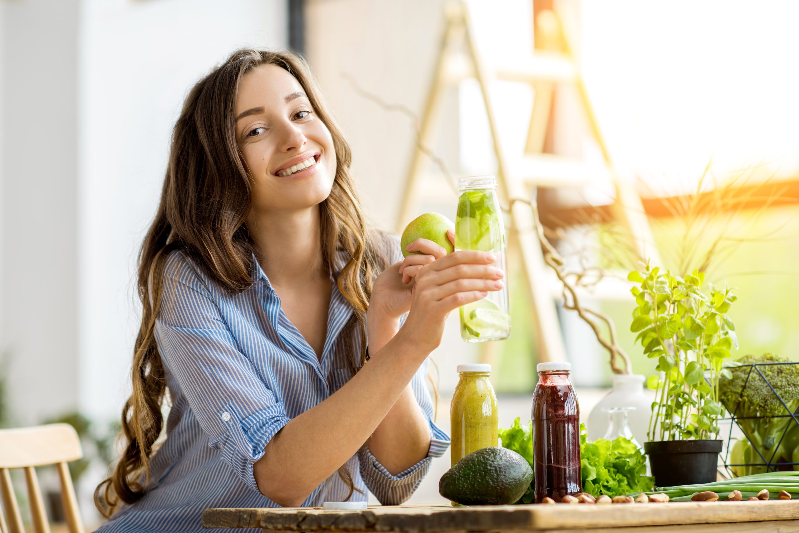 The Top 3 Essentials to Balance Hormones Naturally | balance hormones naturally woman sitting with drinks and healthy green food at home scaled balance hormones naturally - woman sitting with drinks and healthy green food at home