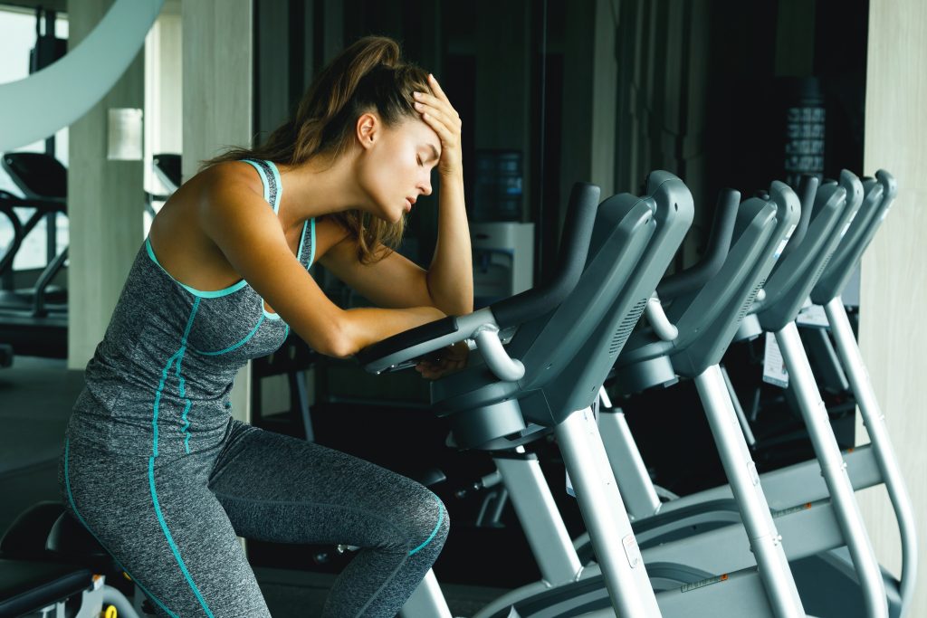 How to Give Up Chronic Cardio Without Gaining Weight | Chronic Cardio Woman on the stationary bike with overtraining symptoms Chronic Cardio - Woman on the stationary bike with overtraining symptoms