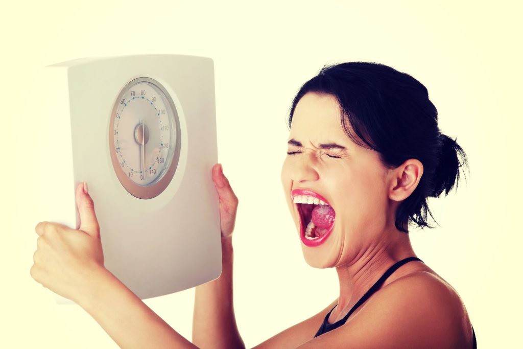 Not Eating Enough & Weight Gain: 10 Signs You’re Not Eating Enough | Not Eating Enough Frustrated young woman with scale Not Eating Enough - Frustrated young woman with scale