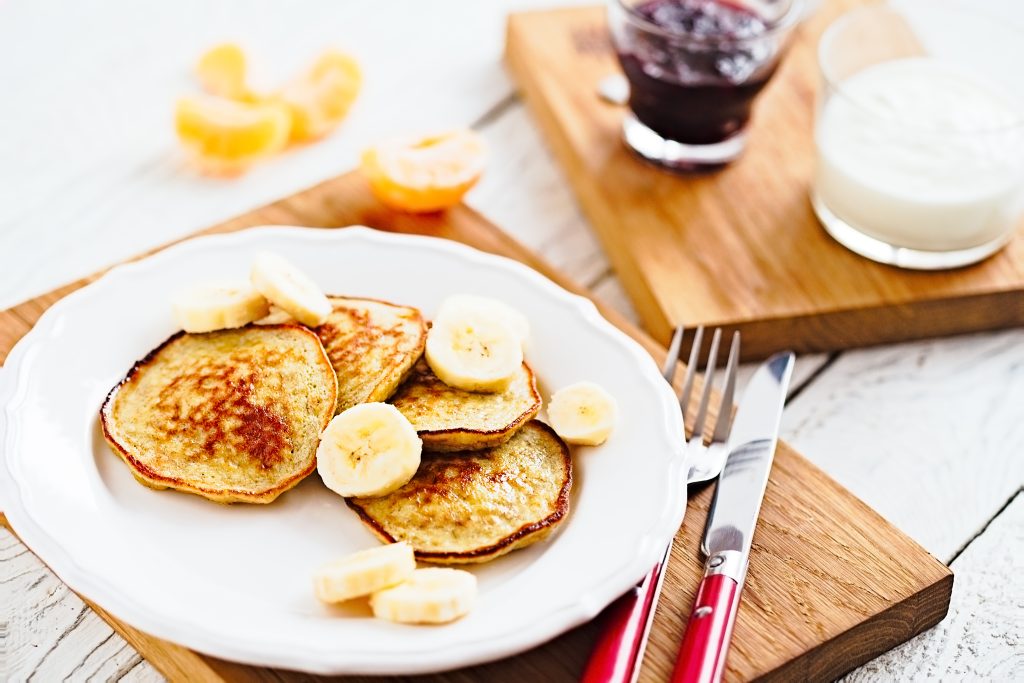 Have You Accidentally Eaten Foods That Cross-React with Gluten? Avoid These Top 10 Triggers | foods that cross react with gluten pancakes with banana and coconut on a white plate with red fork and knife foods that cross-react with gluten - pancakes with banana and coconut on a white plate with red fork and knife