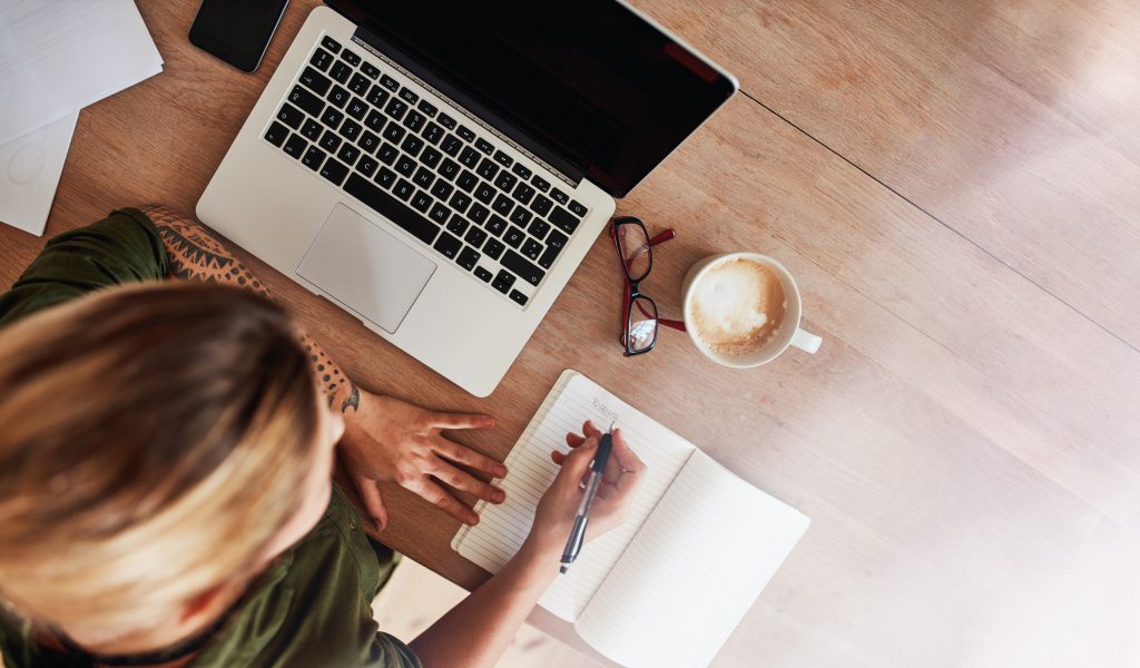 Spark Joy: The #1 Health Hack No One is Talking About to Heal Your Body with Your Mind | Spark Joy woman sitting at table with laptop and coffee writing on notebook Spark Joy - woman sitting at table with laptop and coffee writing on notebook