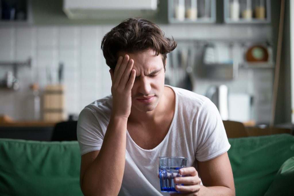 The 7 Gut Types: Which One Are You? | gut types Young man suffering from strong headache or migraine sitting with glass of water gut types - Young man suffering from strong headache or migraine sitting with glass of water