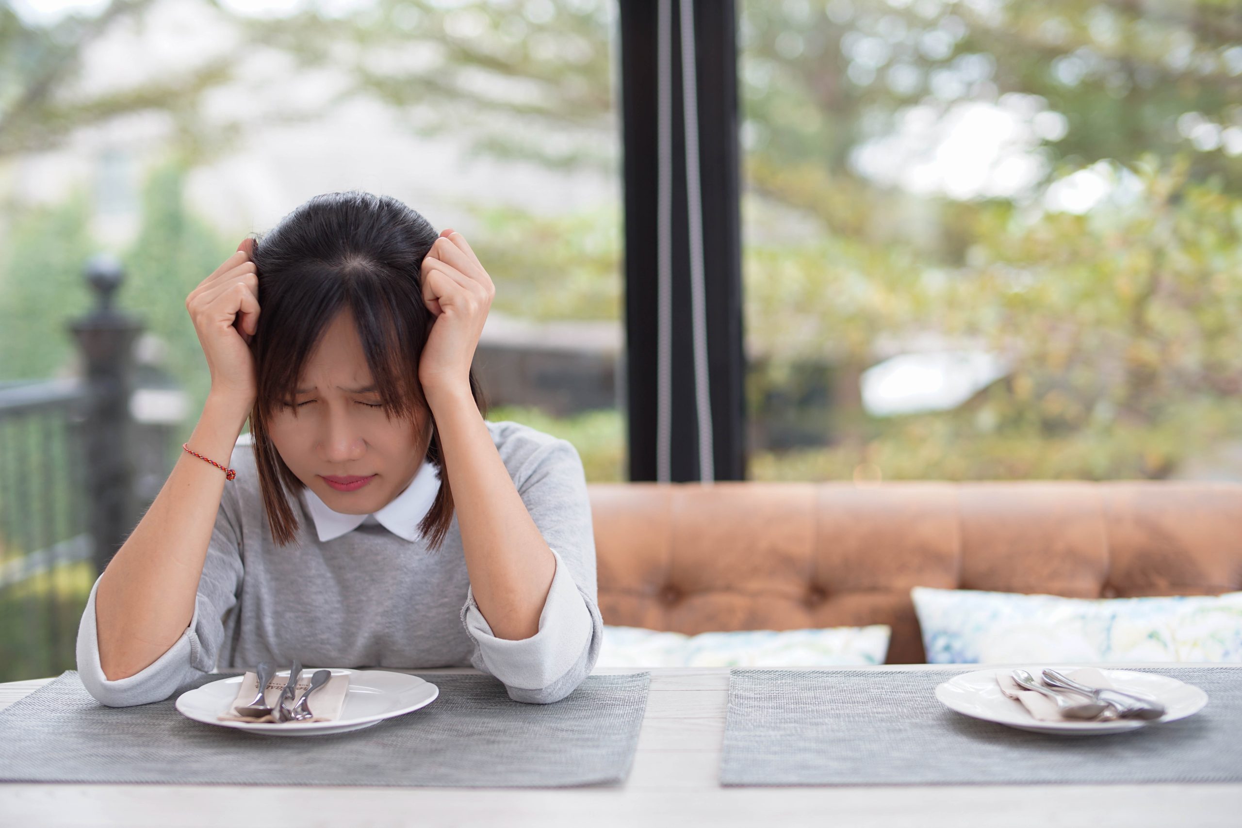 10 Health Issues That Can Happen After Eating Disorders + How to Heal | Eating Disorders Woman sitting alone at dining table getting stressful and headache scaled Eating Disorders - Woman sitting alone at dining table getting stressful and headache