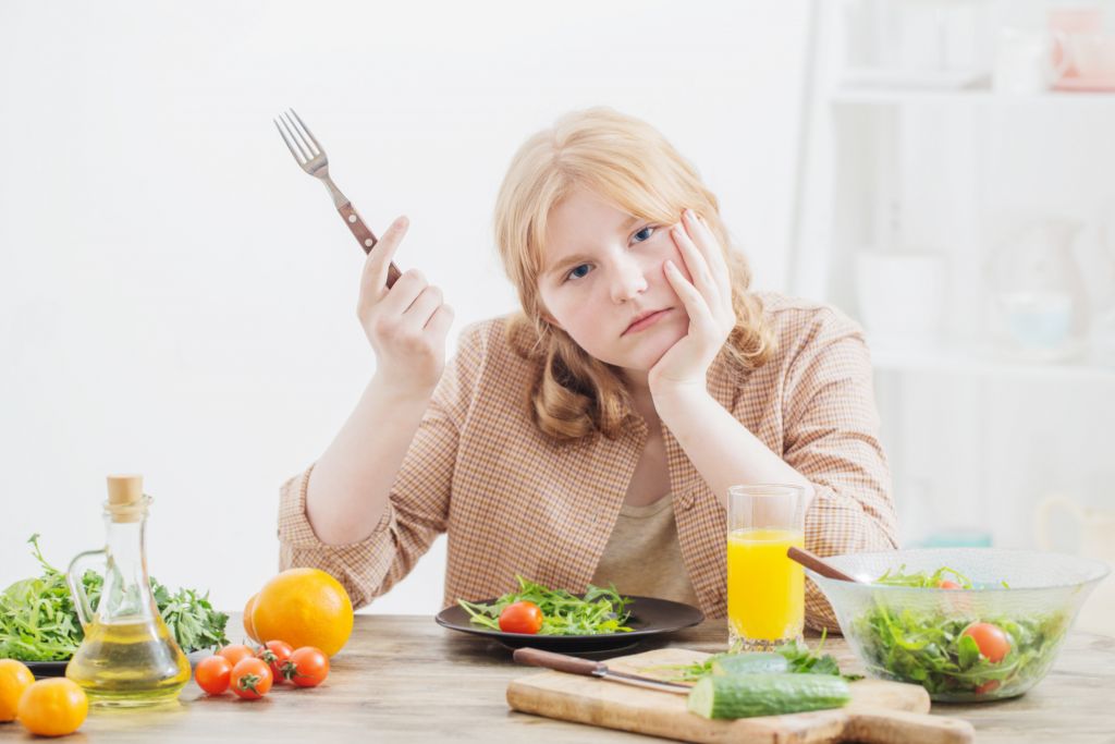 Plant Based Diet Constipation & Bloating: Why it Happens + 3 Remedies to Kick It | Plant Based Diet Constipation young woman holding a fork unhappy with her meal Plant Based Diet Constipation - young woman holding a fork unhappy with her meal